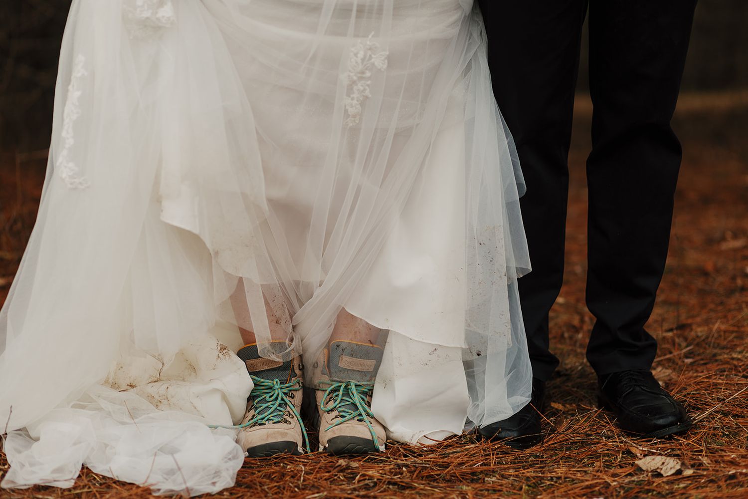 A wedding photo showing green sneakers peeking out beneath a white wedding dress next to formal black shoes.