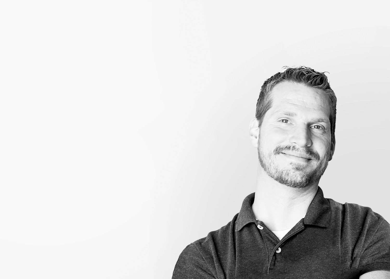 Black and white professional headshot of a smiling person wearing a dark polo shirt against a white background.
