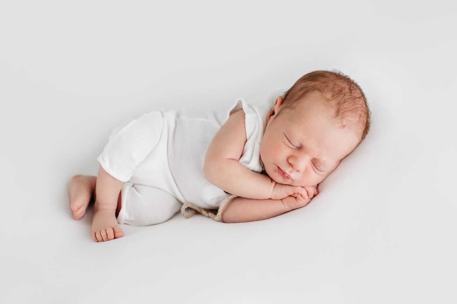 Sleeping newborn in white onesie on light background.