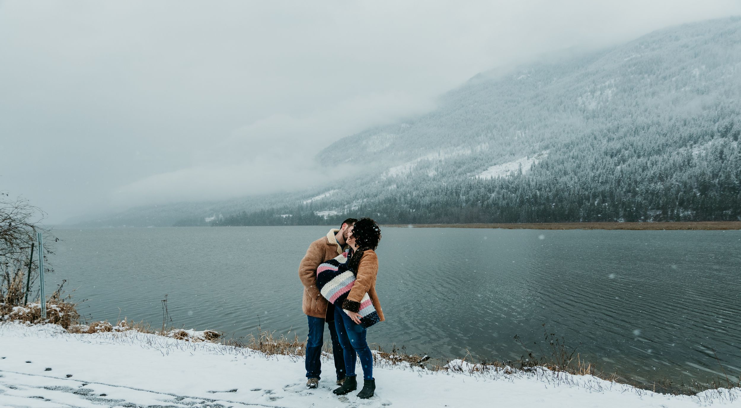 Family with baby share a kiss next to frozen lake
