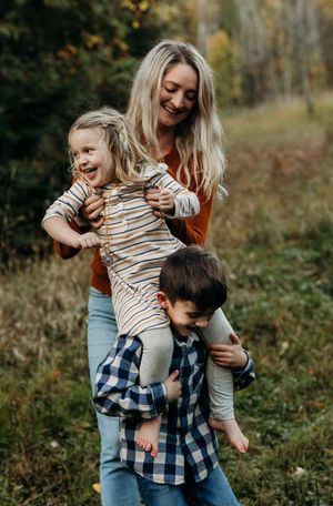 Mum helping her son give piggy back ride to her daughter