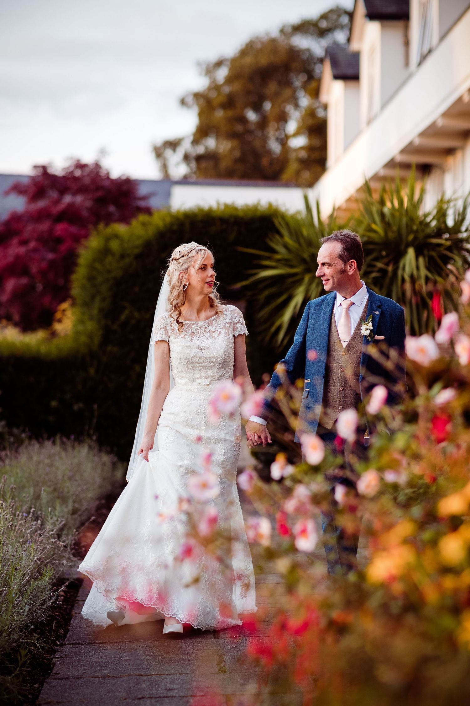 A romantic garden path lined with colorful flowers and modern architecture in the background.