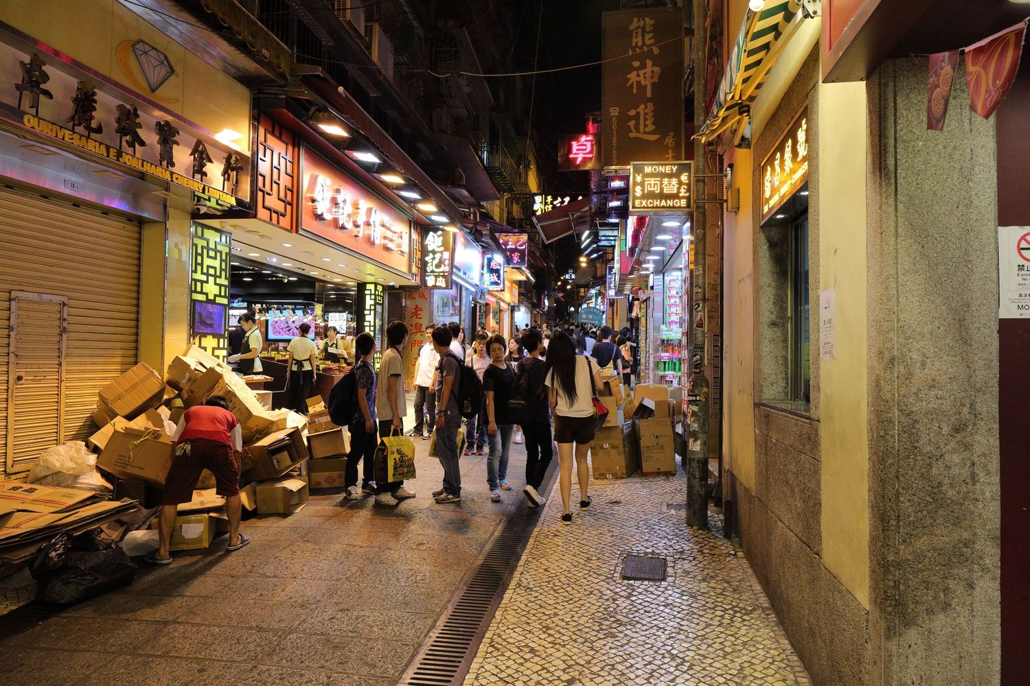 Bustling night street in Macau with neon signs and people walking along narrow alley with traditional storefronts.