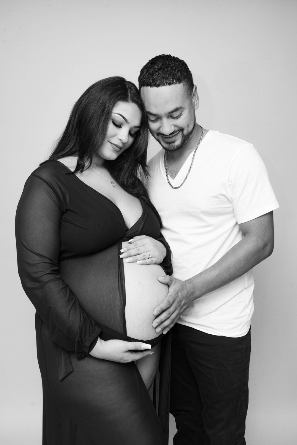 Black and white maternity photo of a couple lovingly looking down at a pregnant belly together.