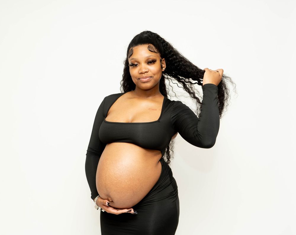 Pregnant Black woman in black crop top outfit cradles baby bump while posing for maternity portrait.