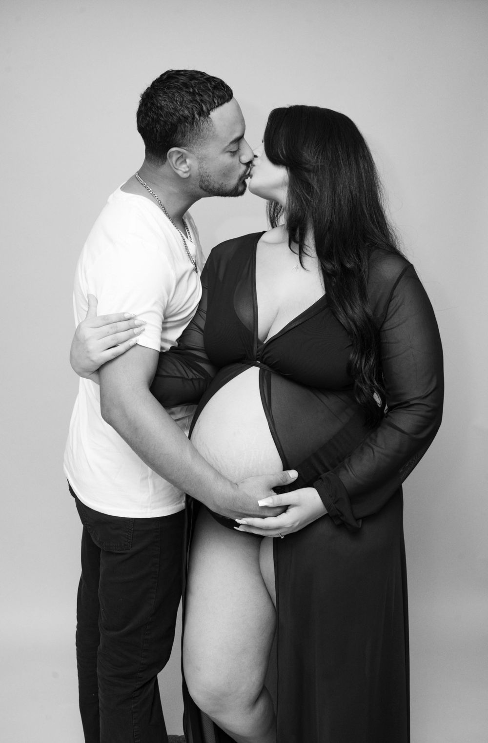 Black and white maternity photo of a couple kissing while cradling a pregnant belly.