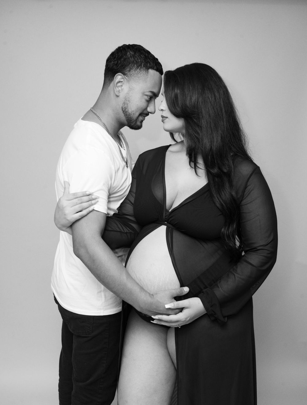 Black and white maternity photo of a couple touching foreheads while holding a pregnant belly.