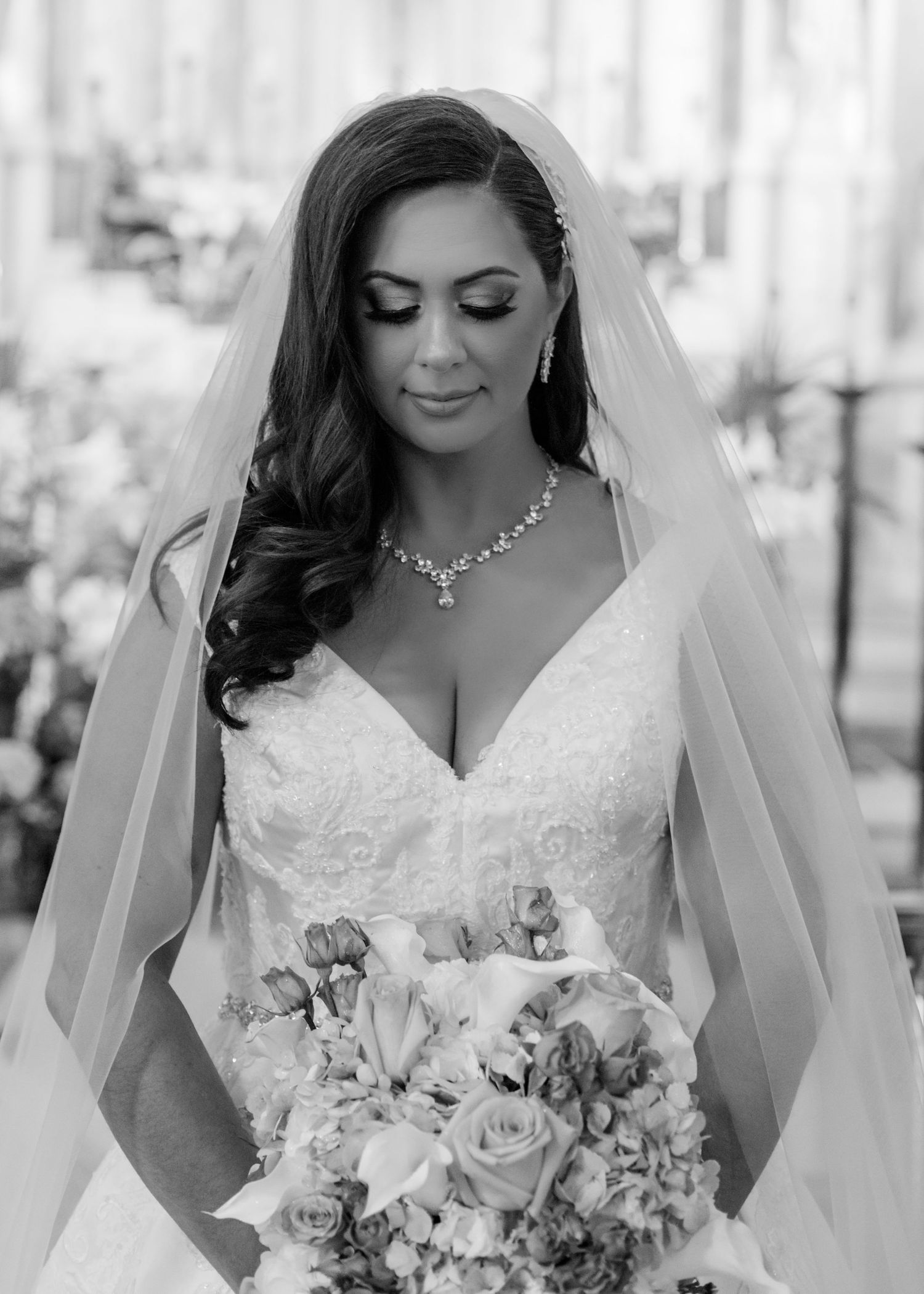 A bridal portrait in black and white showcasing an elegant lace wedding dress and floral bouquet.