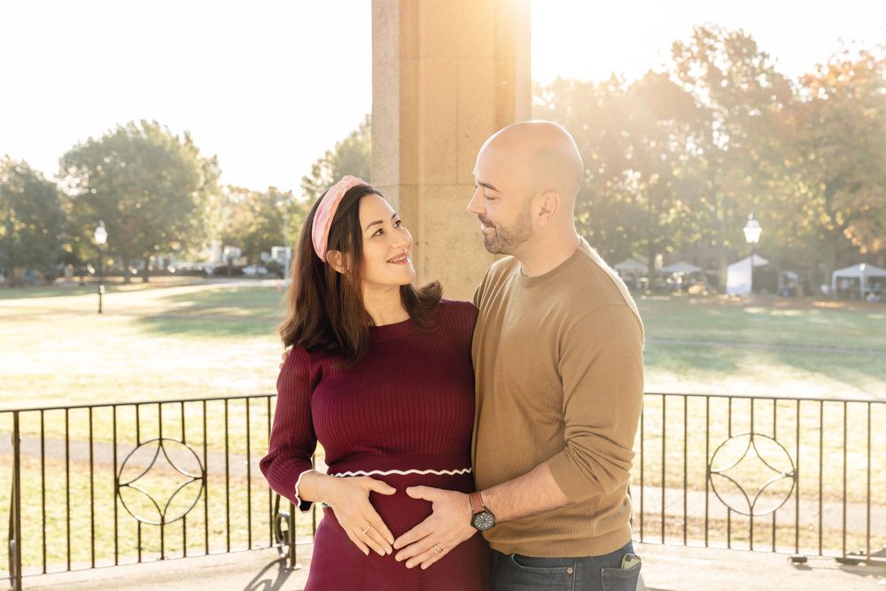 Expectant couple shares intimate moment at sunset in front of decorative fence.