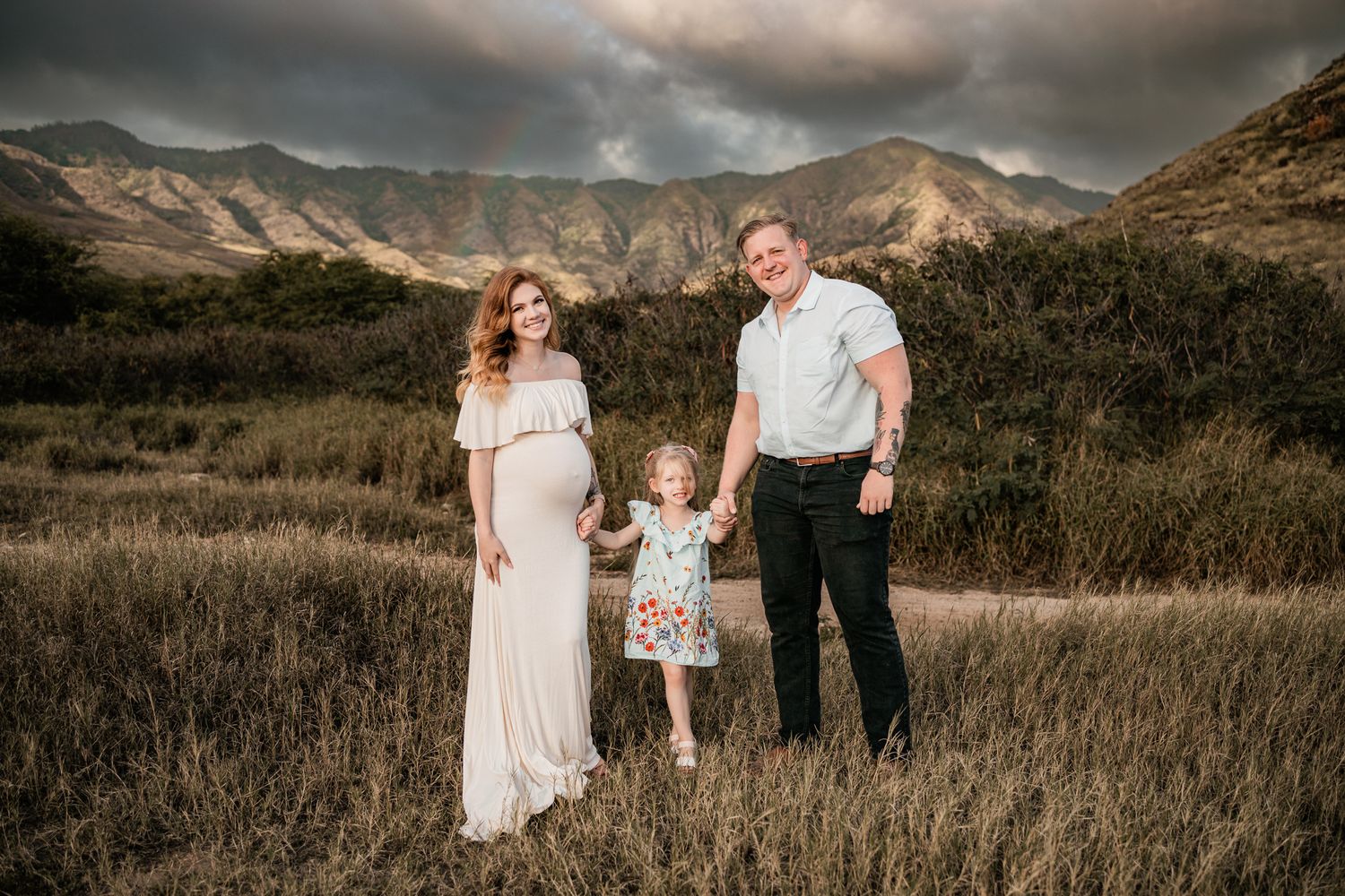 Family poses together in field with dramatic mountain landscape at sunset.
