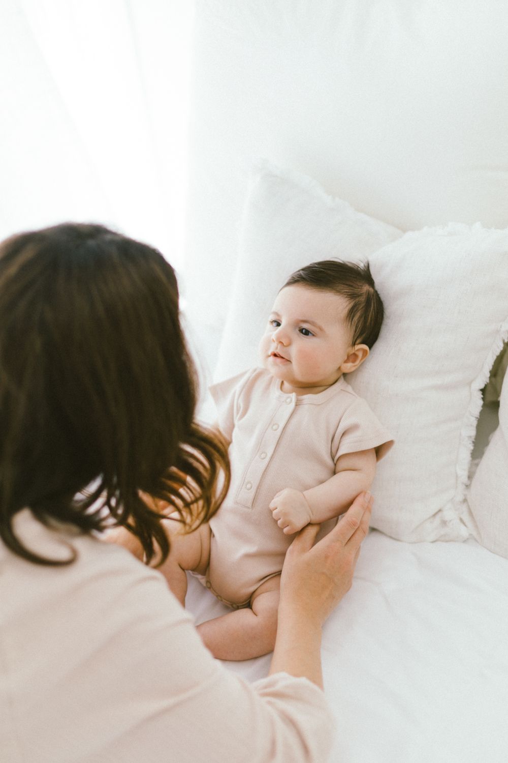 Parent and infant share gentle moment together on white bedding.
