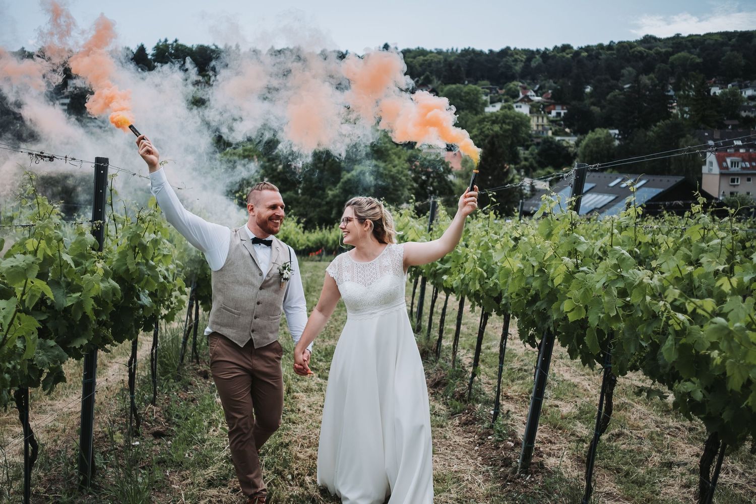 Couple celebrating with colorful smoke bombs in a vineyard setting.