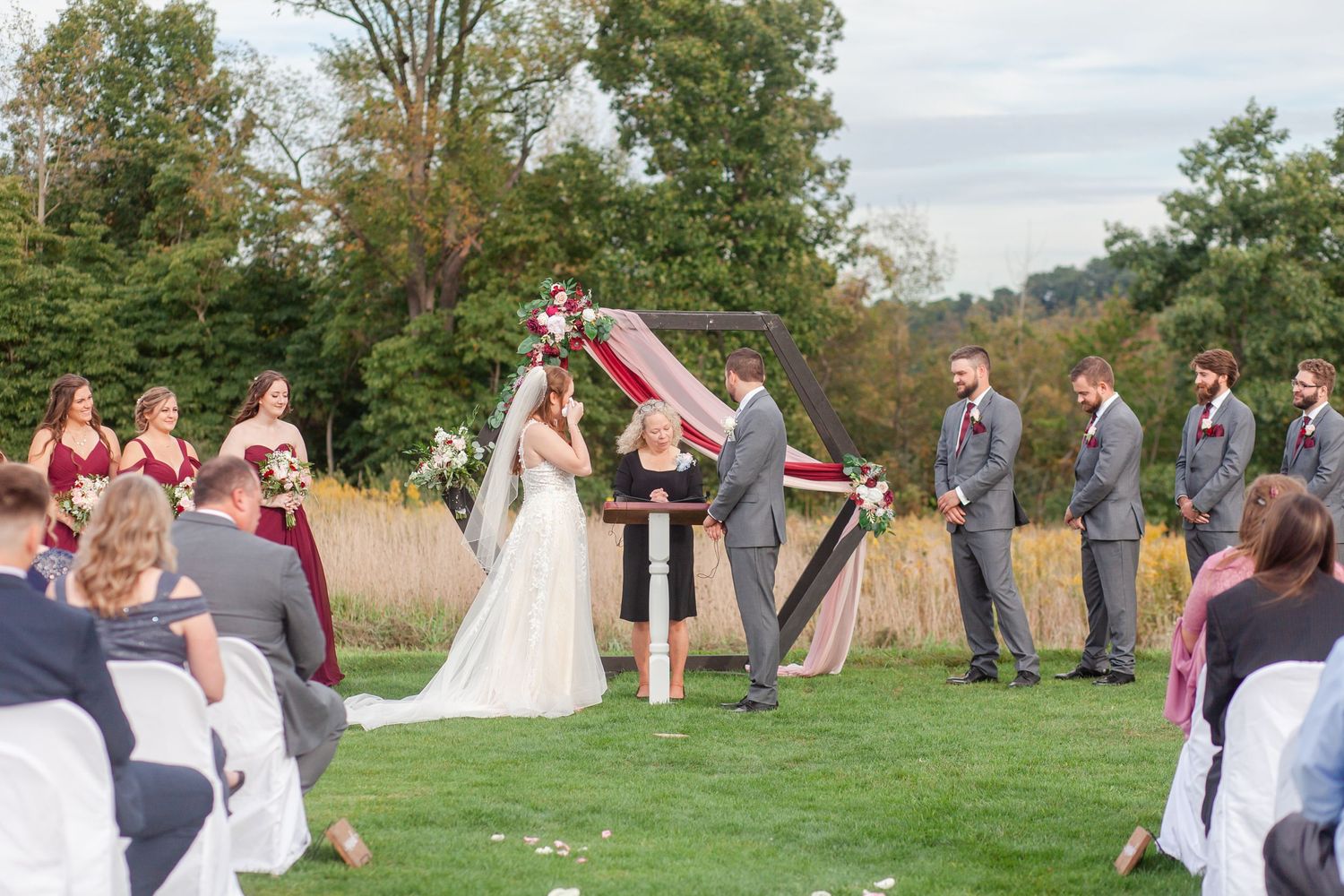 An outdoor wedding ceremony setup with white chairs and floral decorations against a natural landscape backdrop.