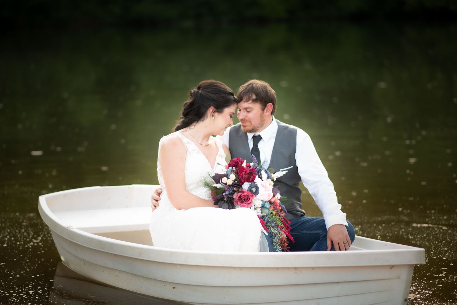 Newlyweds share romantic moment in white rowboat on peaceful lake.