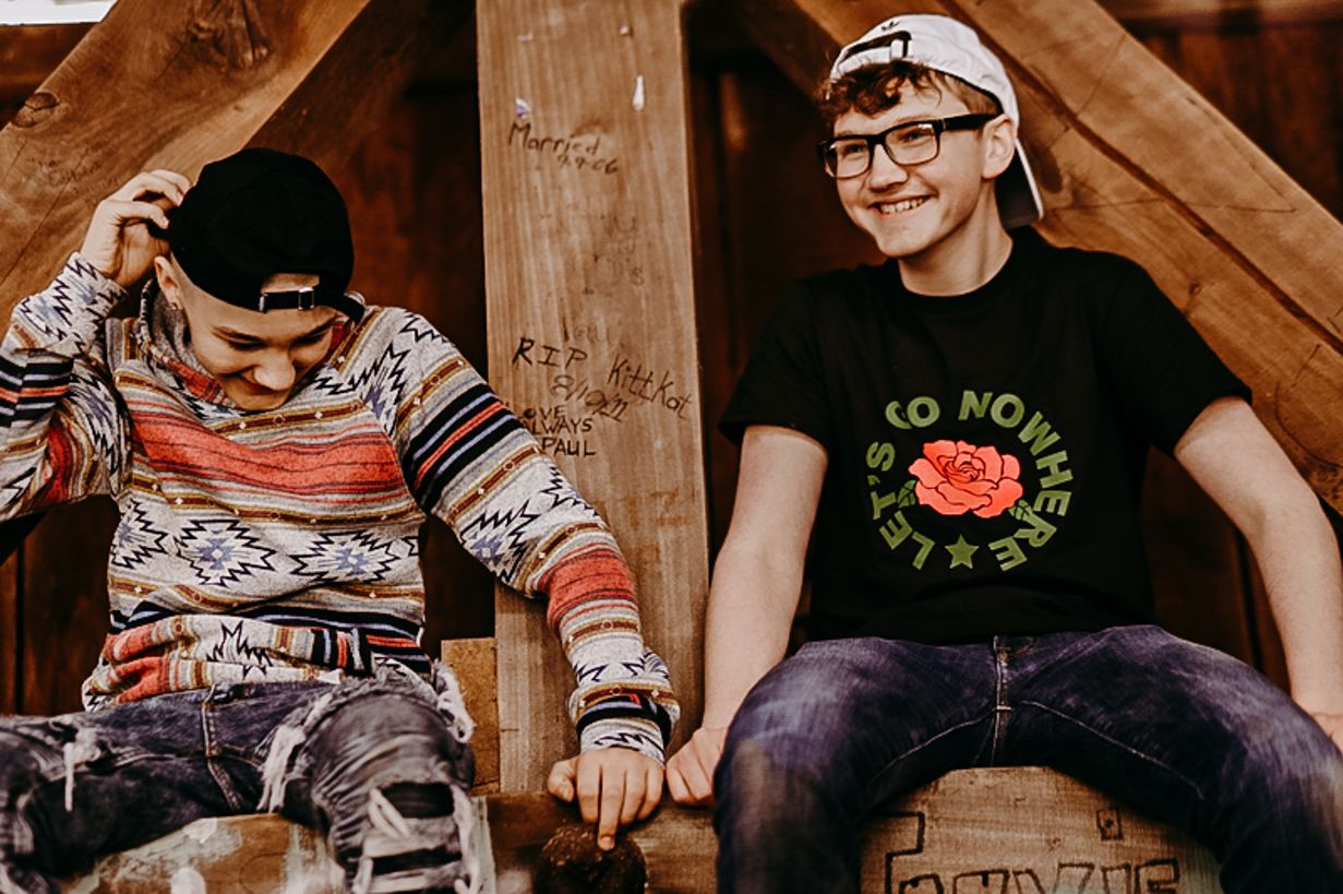 Two people sitting and laughing together on wooden structure wearing casual clothes.