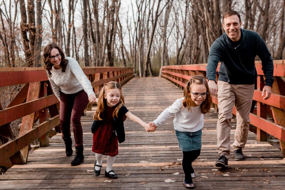A family runs and plays together on a wooden bridge in the forest.