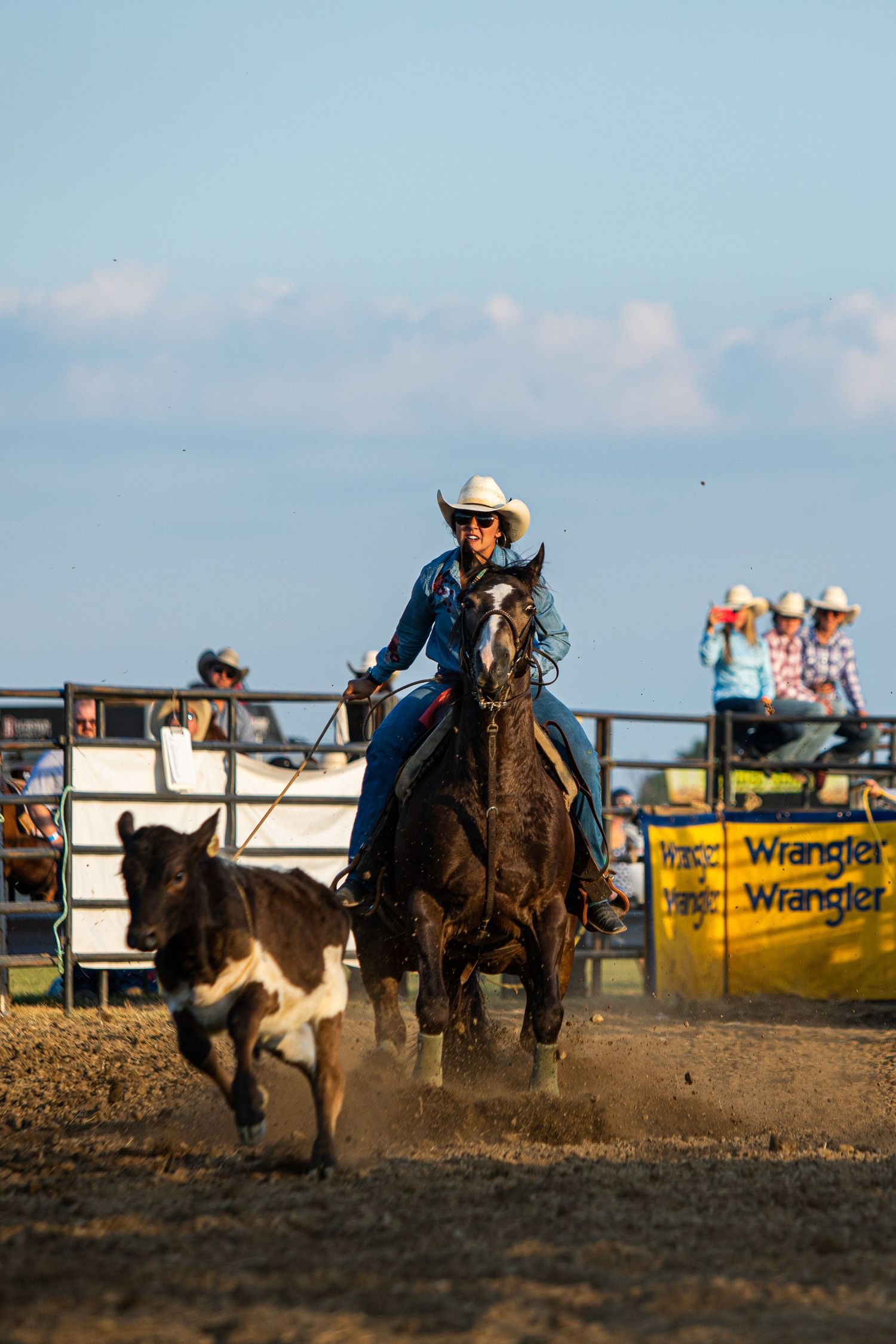 Rodeo action shot of riders racing across dusty arena at sunset.