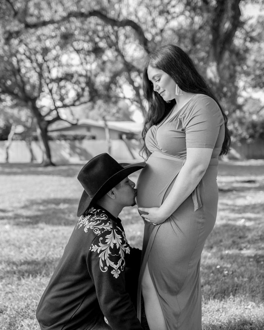 Black and white maternity moment captured under trees in a park setting.