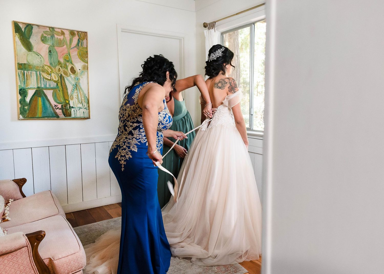 An elegant wedding dress being fitted in a bright room with white walls and decorative artwork.