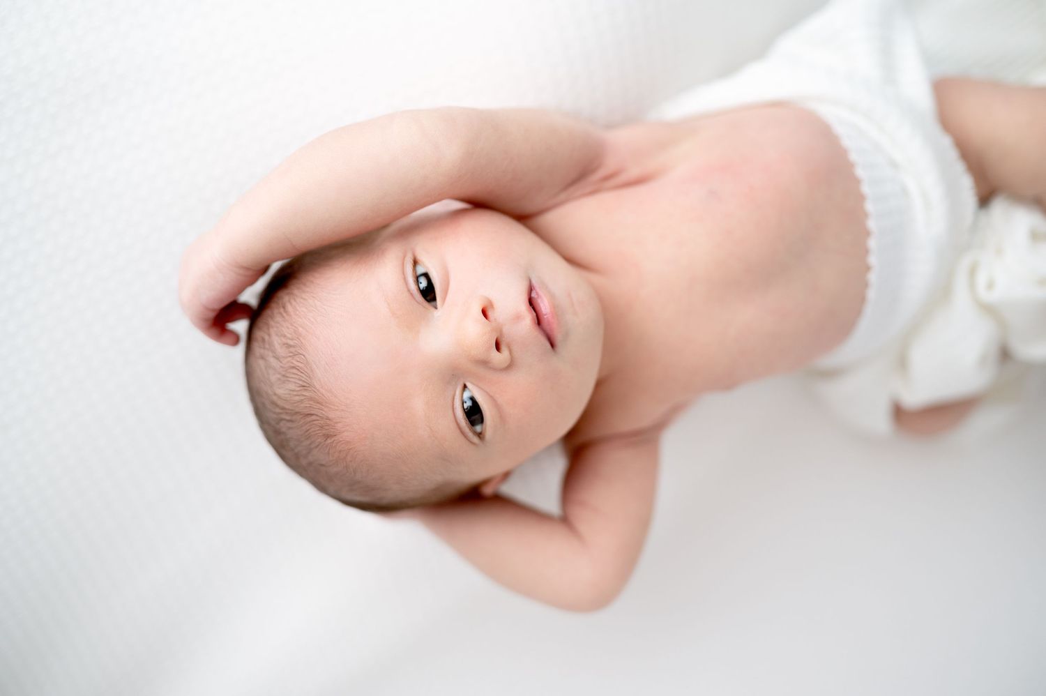 Close-up portrait of alert newborn baby lying on white blanket.
