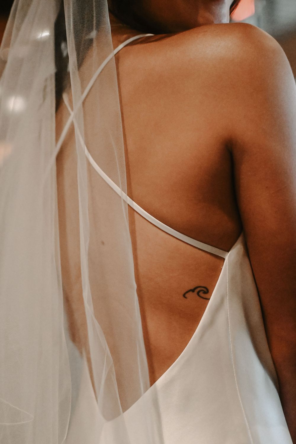 Close up detail of a white wedding dress and small wave tattoo on the back.