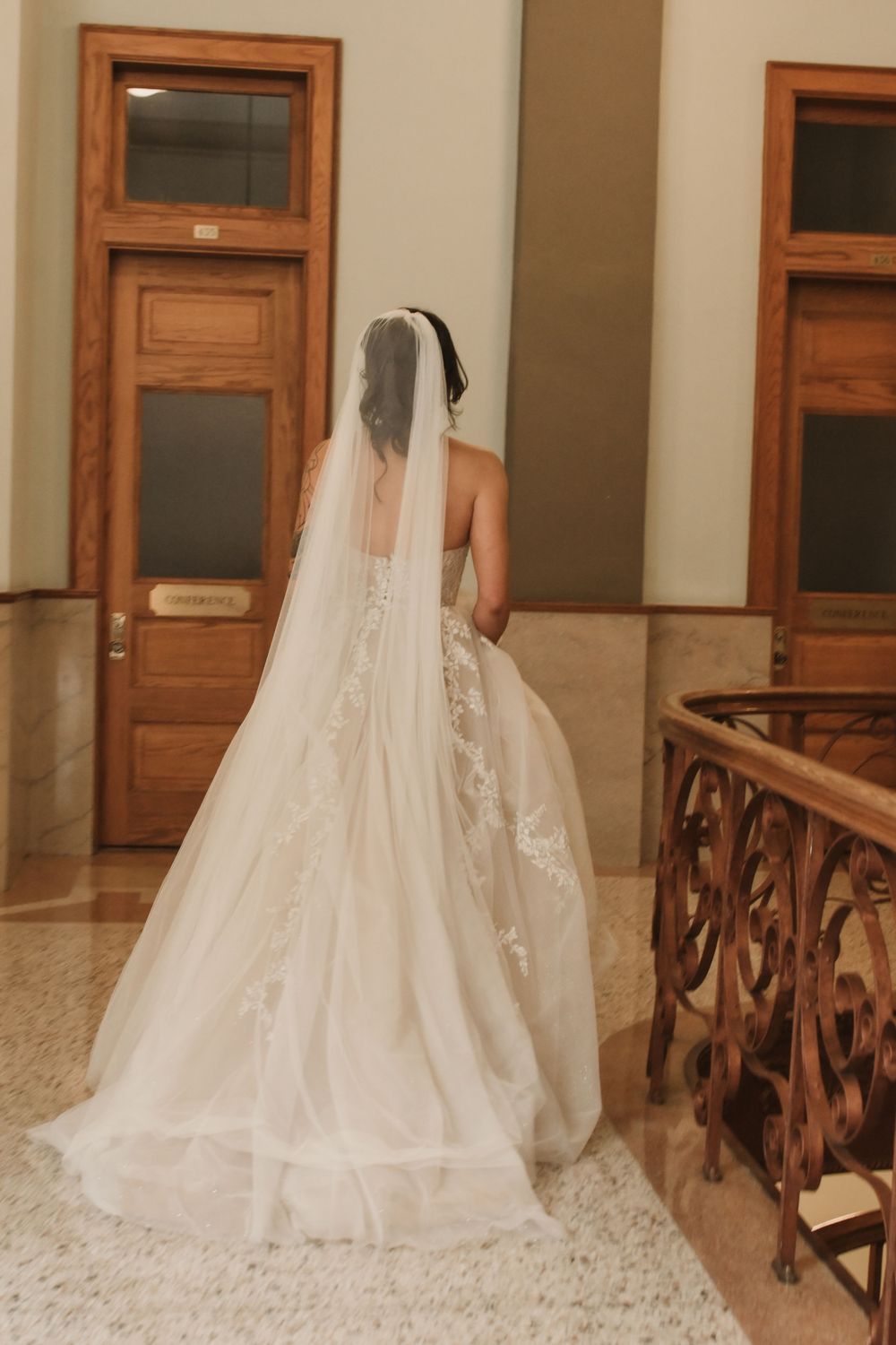 Back view of bride's flowing wedding dress train against ornate wooden railing.