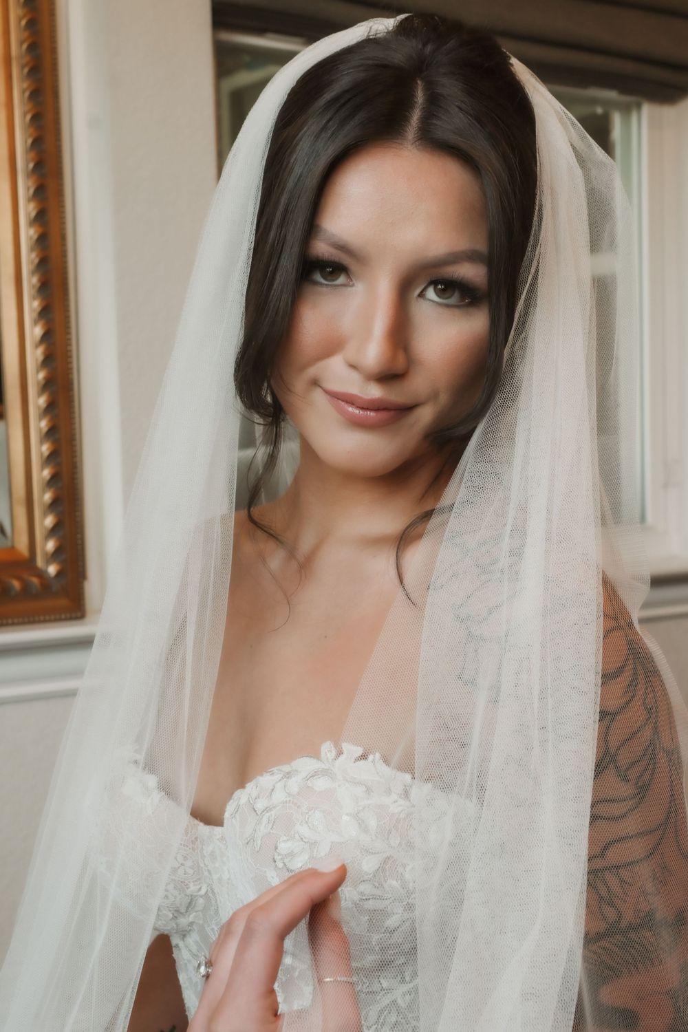 Bride wearing lace wedding dress and veil poses for portrait with soft natural lighting.