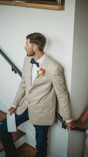 Groom in tan suit jacket descending wooden stairs while reading a letter.