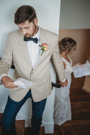 A groom in a beige suit jacket and jeans prepares for the wedding day.