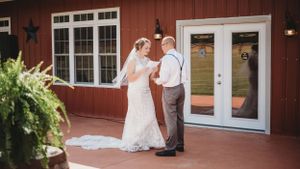 A couple dances together on a porch in front of a red barn during their wedding celebration.