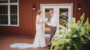 A couple shares a moment outside a red barn building during their wedding day.