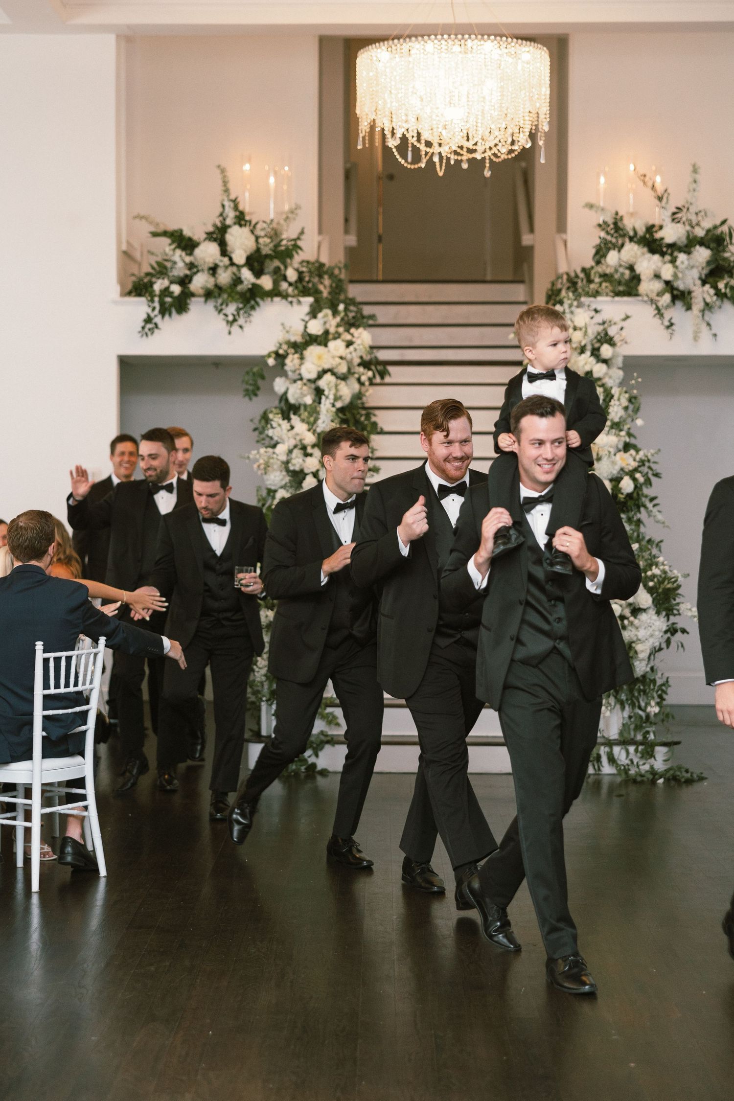 Groomsmen in black tuxedos having fun posing together at an elegant wedding venue.