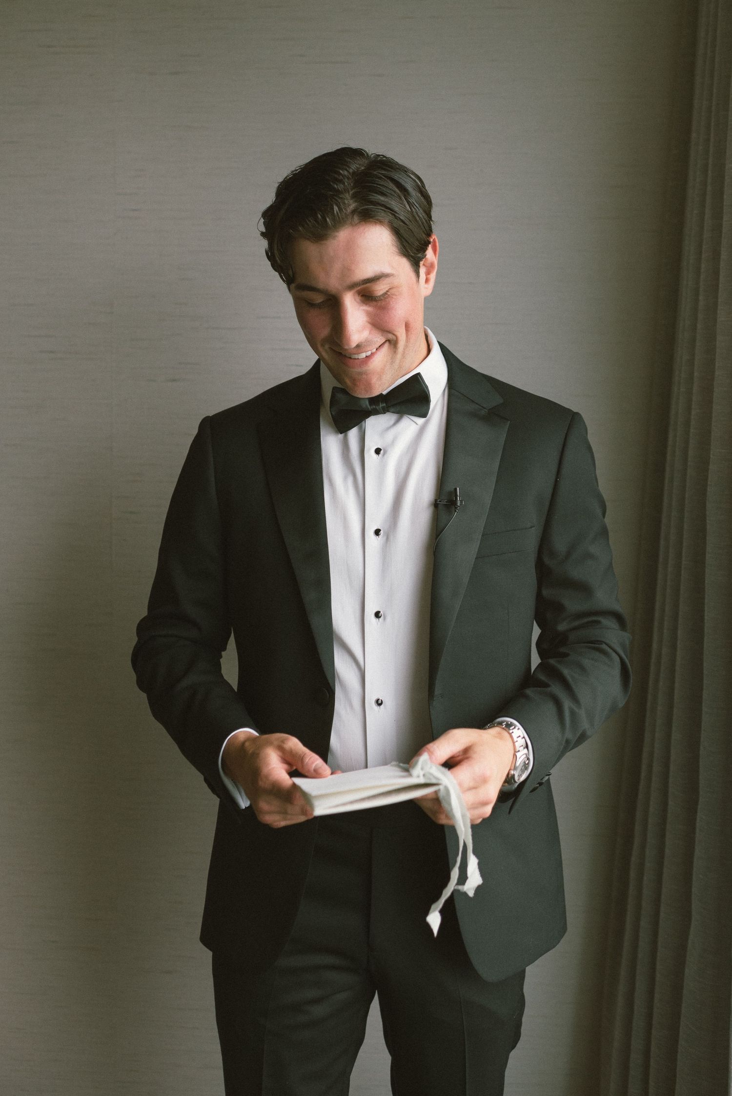 Close-up of groom in black tuxedo adjusting his tie while getting ready.