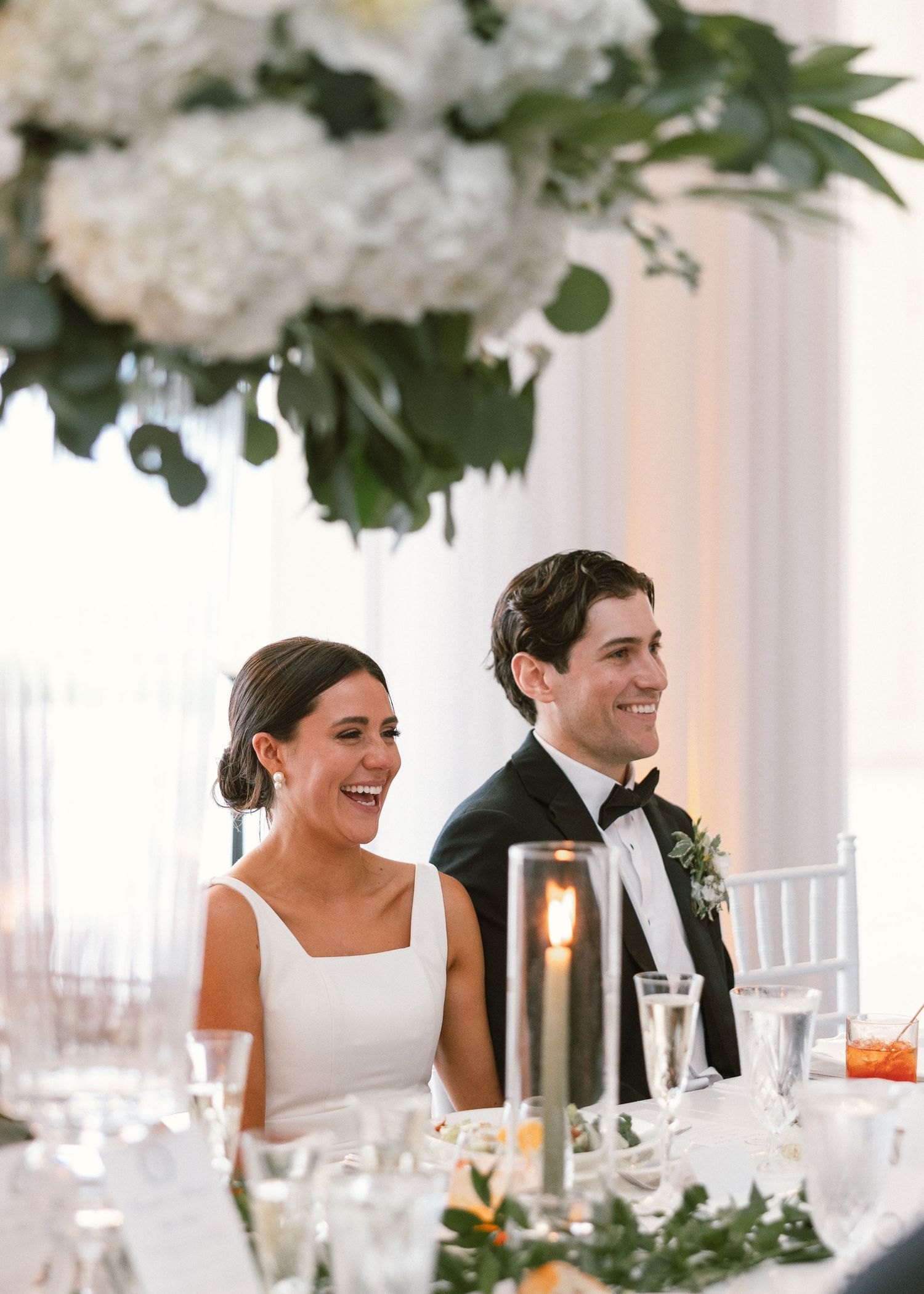 Wedding reception table decorated with white hydrangeas and greenery, with guests enjoying the celebration.