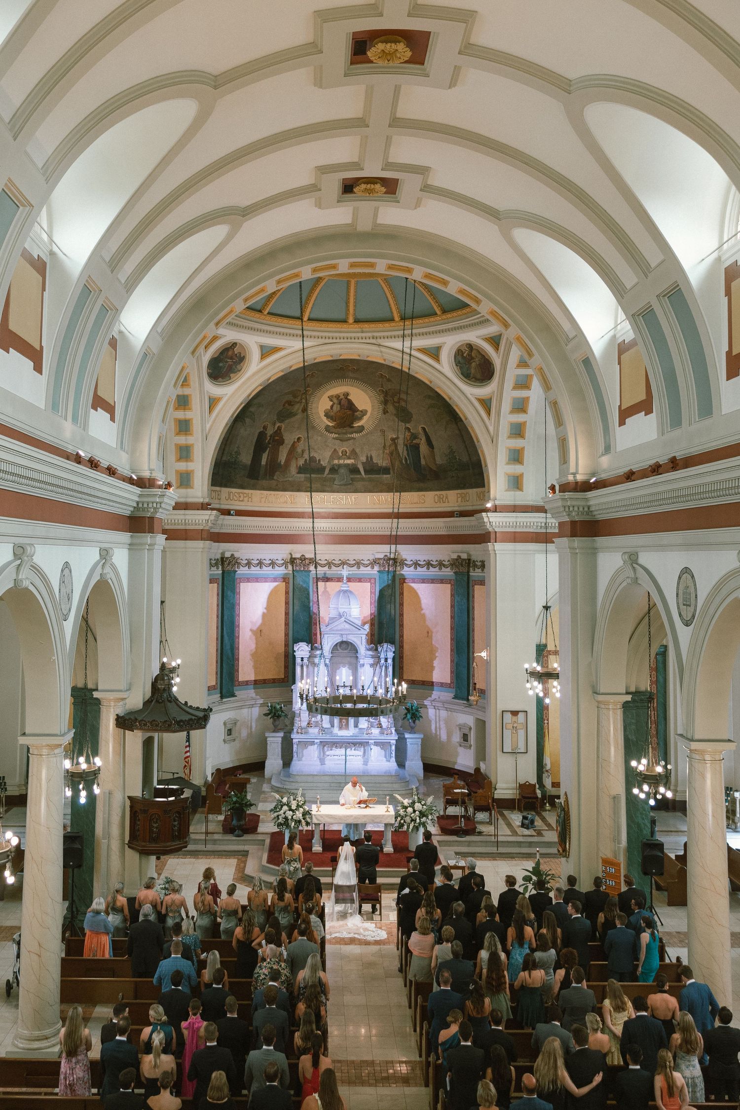 Wide view of packed church sanctuary during wedding ceremony with vaulted ceiling and arched details.