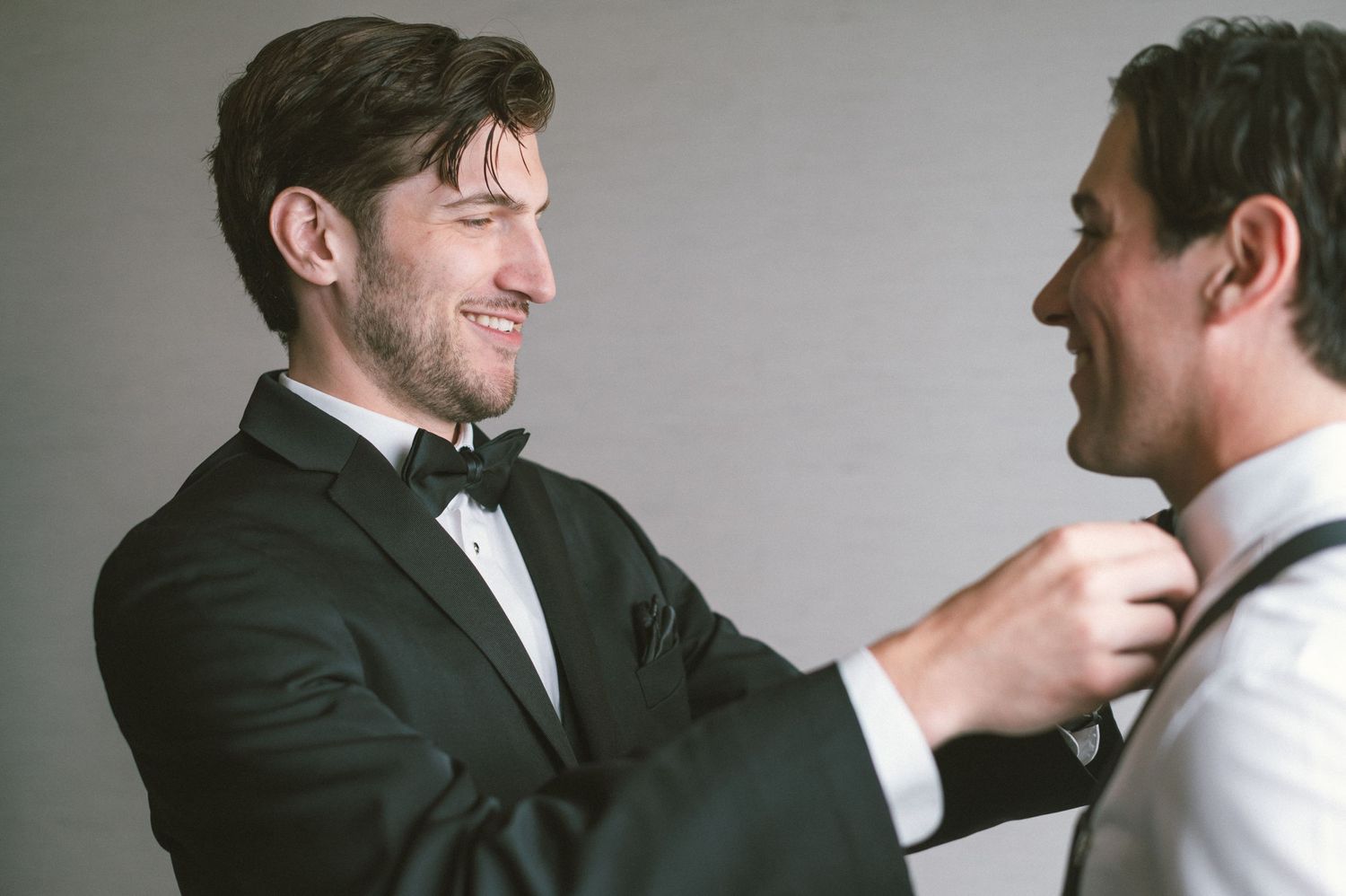 Groomsmen in black tuxedos help adjust each other's bow ties before the ceremony.