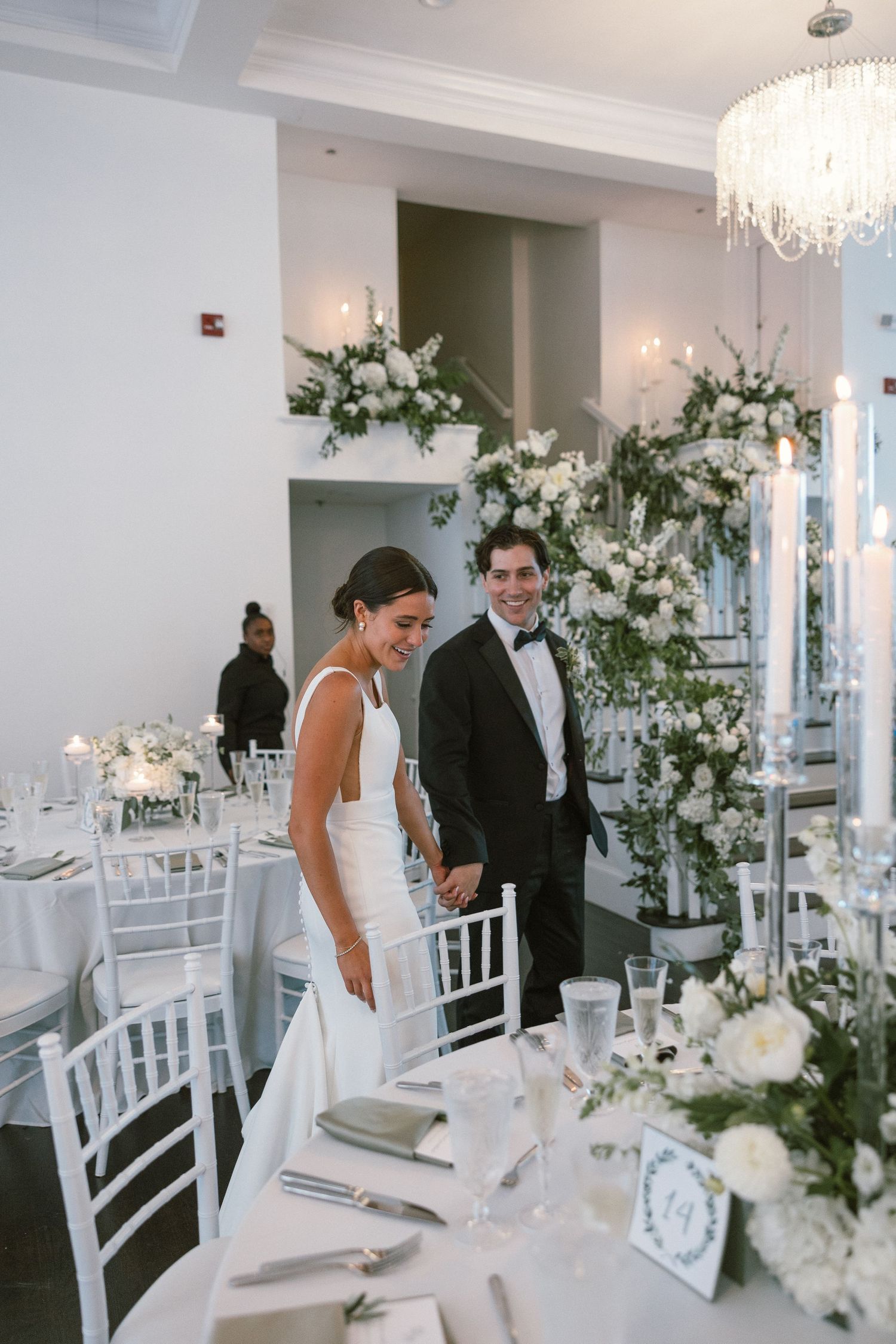 Elegant white wedding reception room with crystal chandeliers and floral centerpieces.