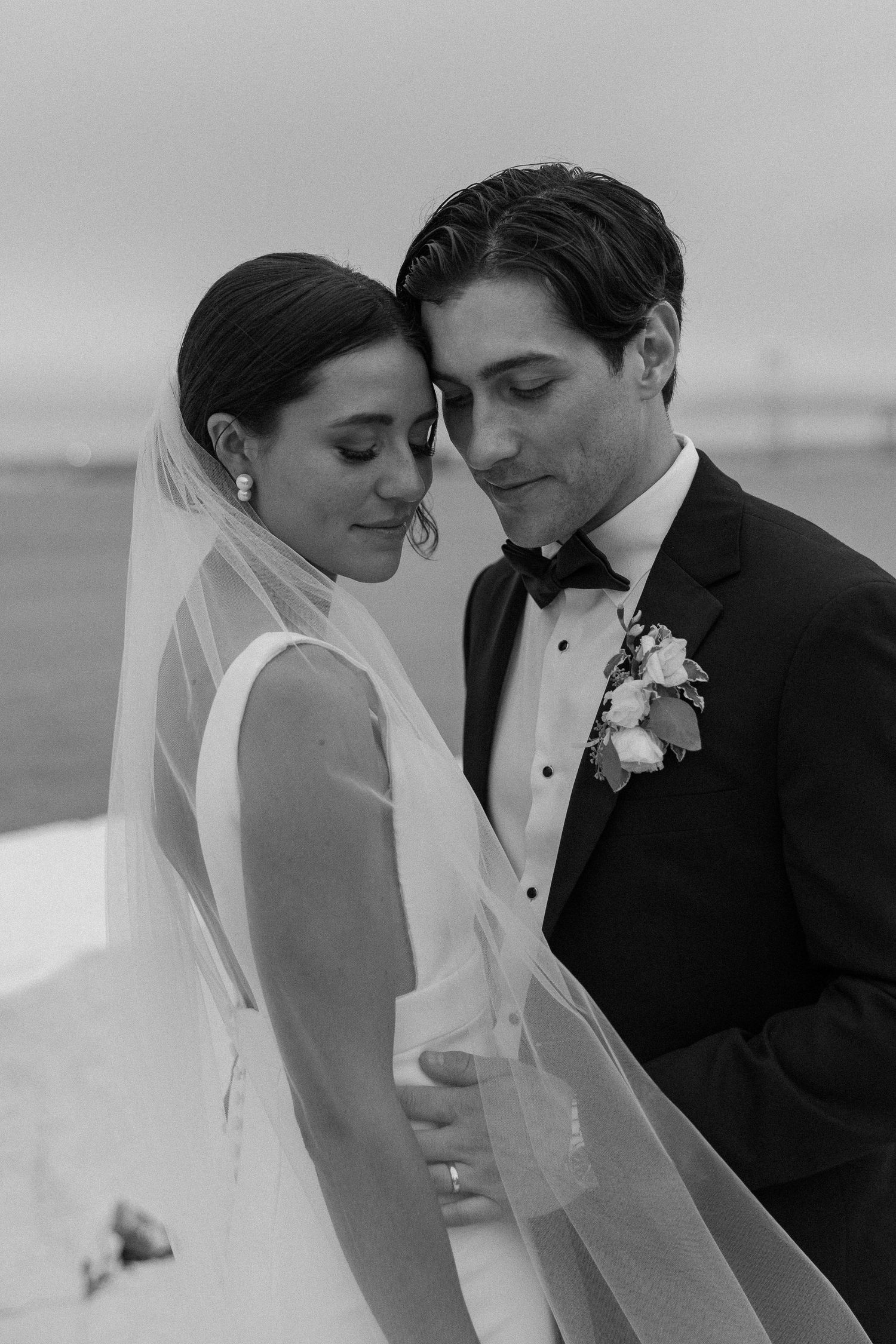 Romantic black and white portrait of a couple on their wedding day by the ocean.