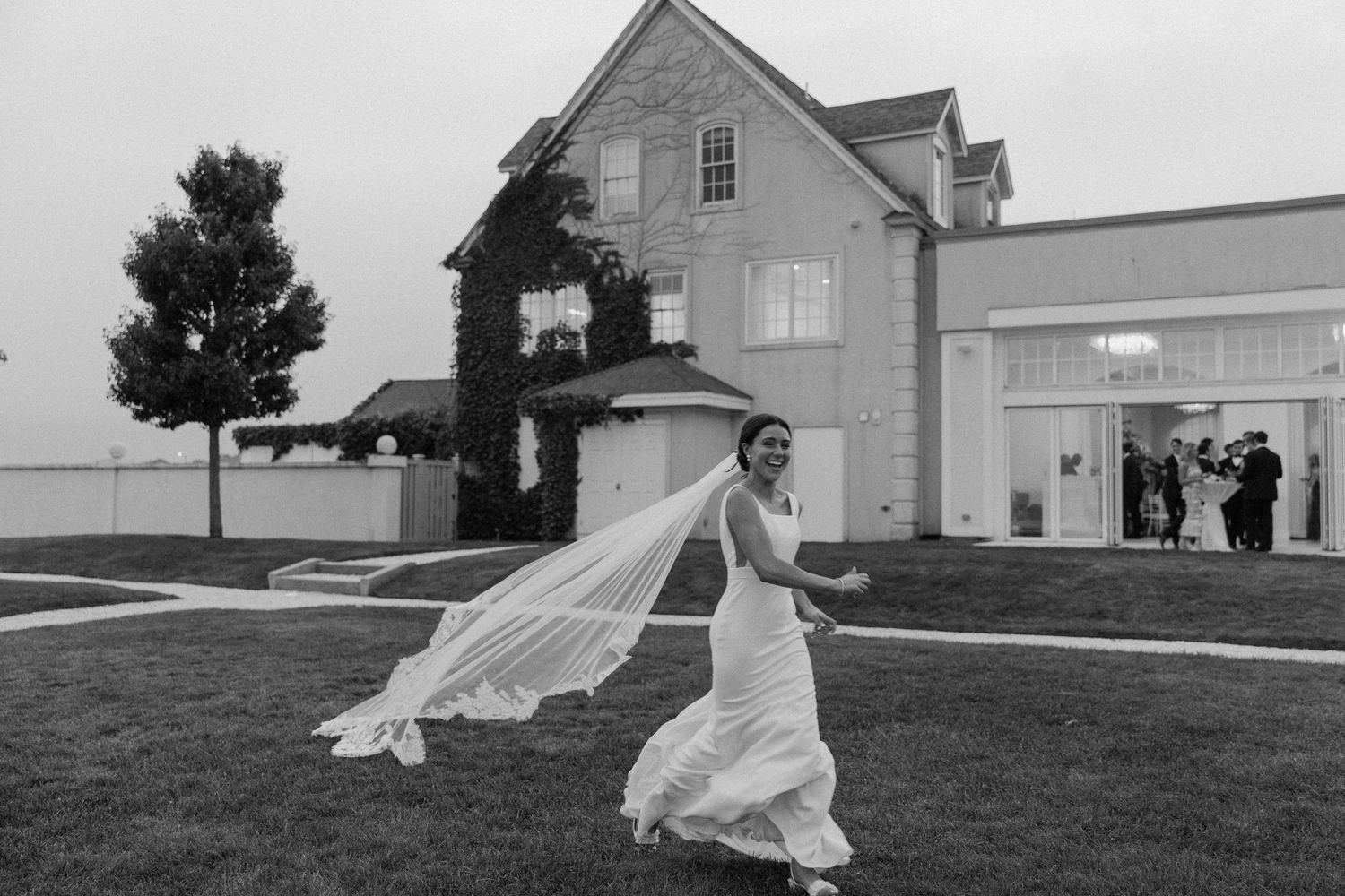 Wedding couple running playfully through a grassy field with flowing dress and veil.