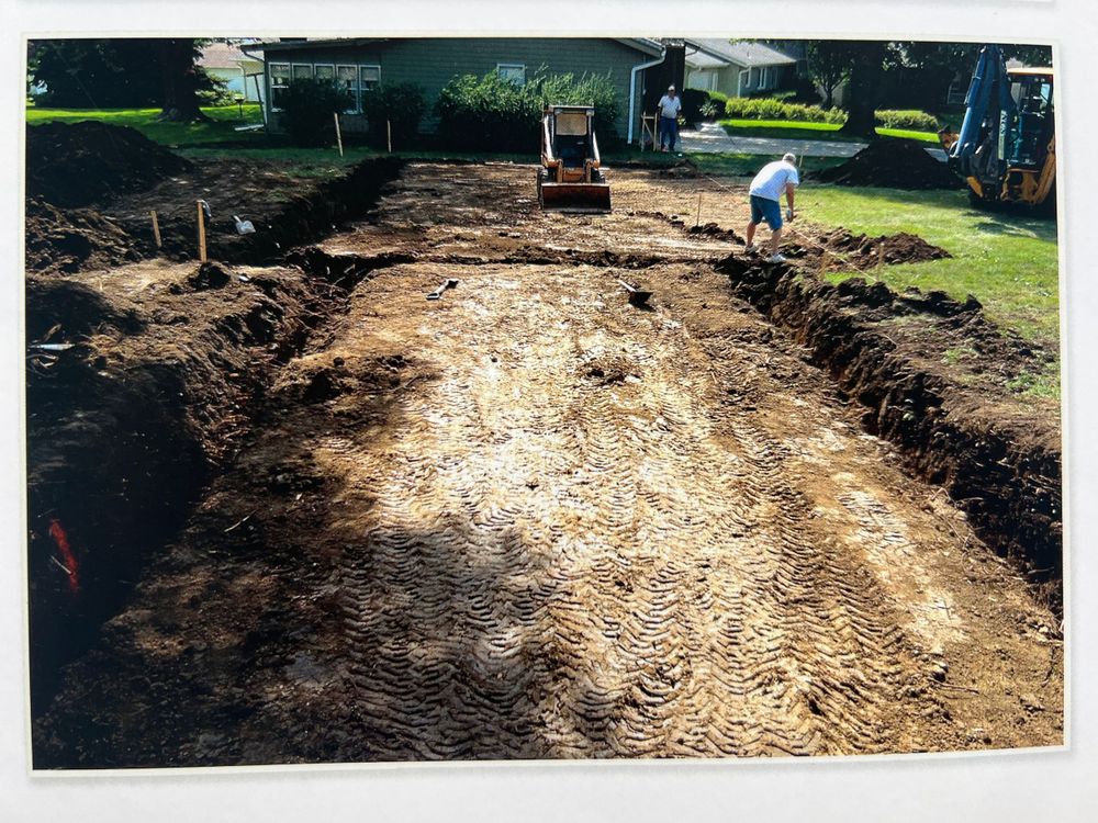 Construction site showing cleared dirt path through wooded area.
