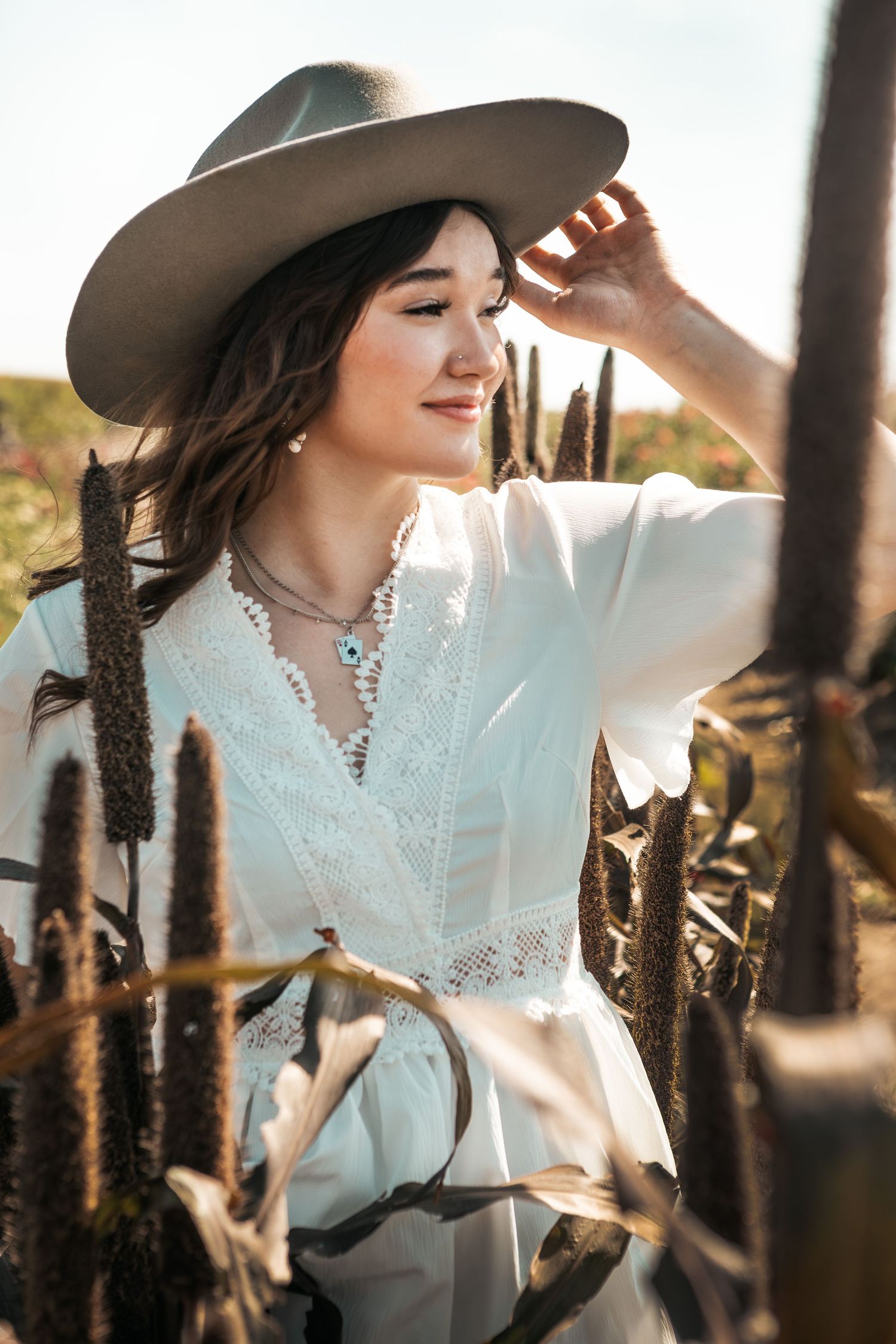 Romantic countryside portrait in white lace dress and brown cowboy hat at sunset.