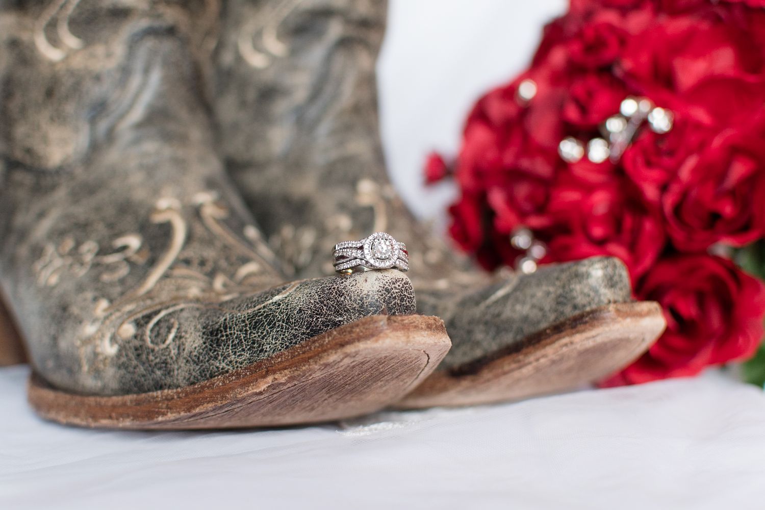 Wedding rings sit atop weathered cowboy boots with red roses in the background.