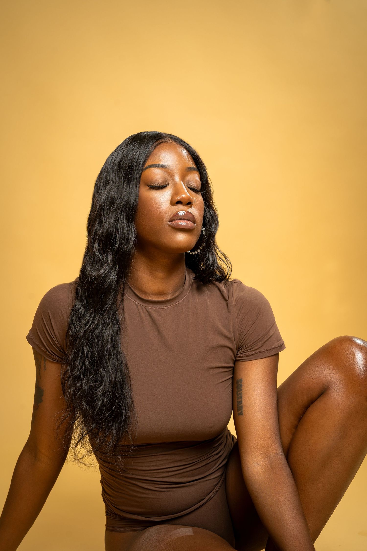 Portrait in brown bodysuit against golden background with soft lighting.