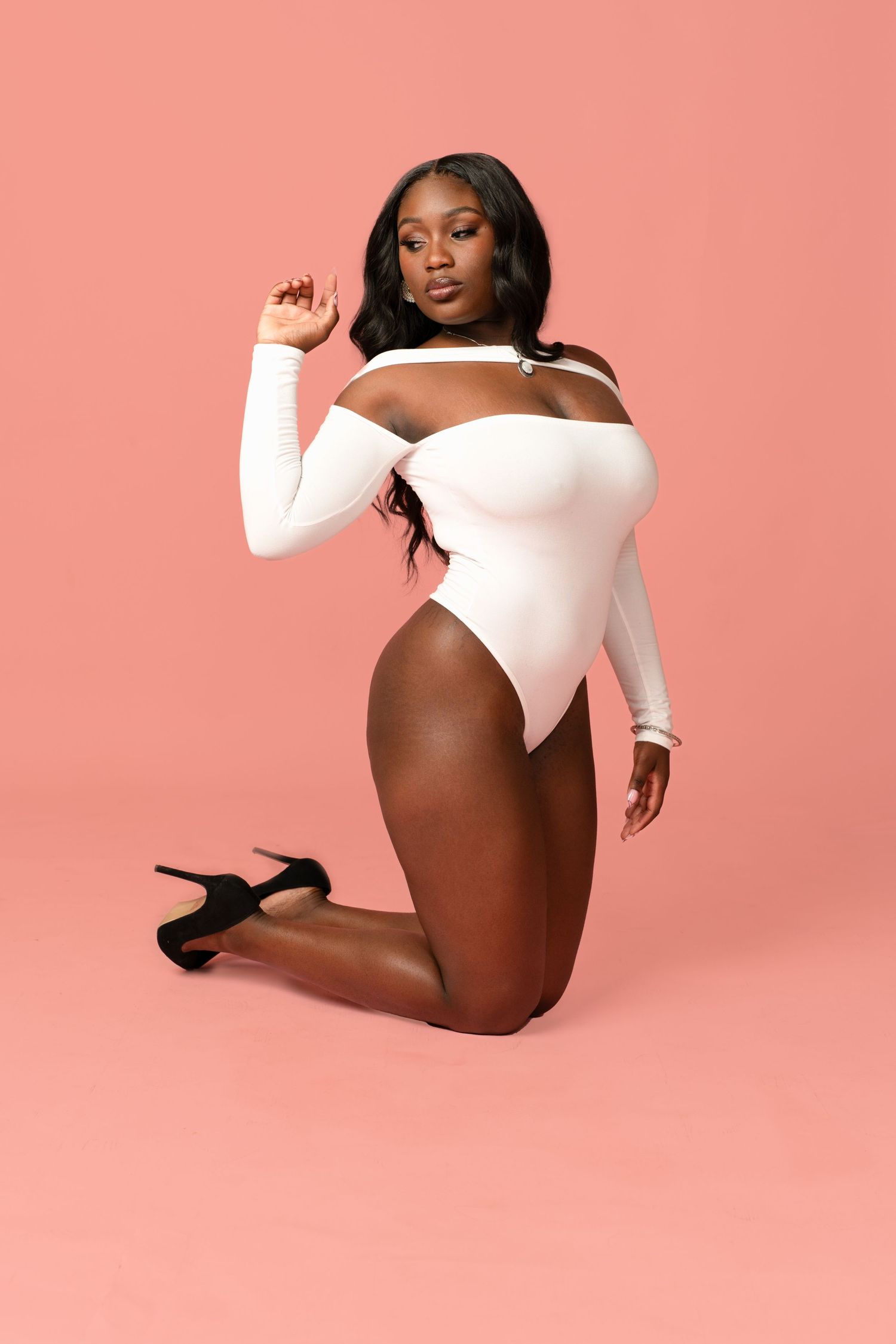 Fashion model in white bodysuit and heels poses against pink backdrop.