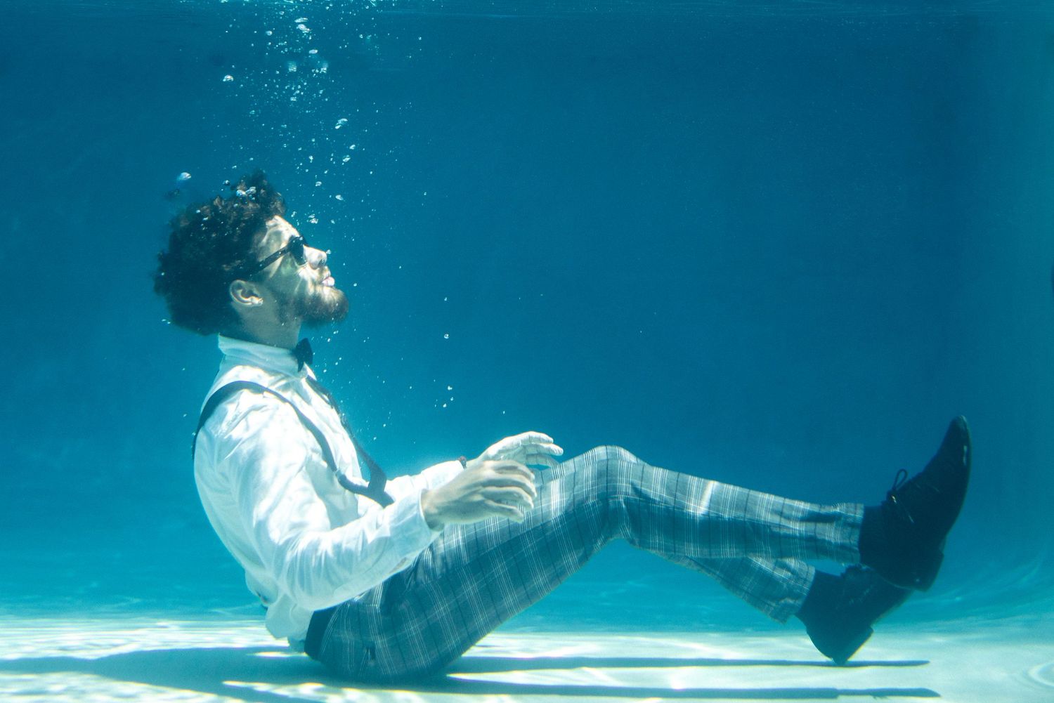Underwater portrait of person in formal attire creating dramatic bubbles and movement.