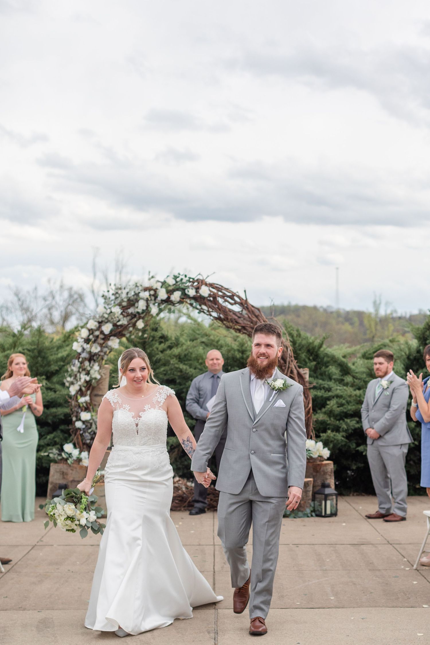 Wedding party in gray suits and mint green dresses dance together on an outdoor patio during a celebration.