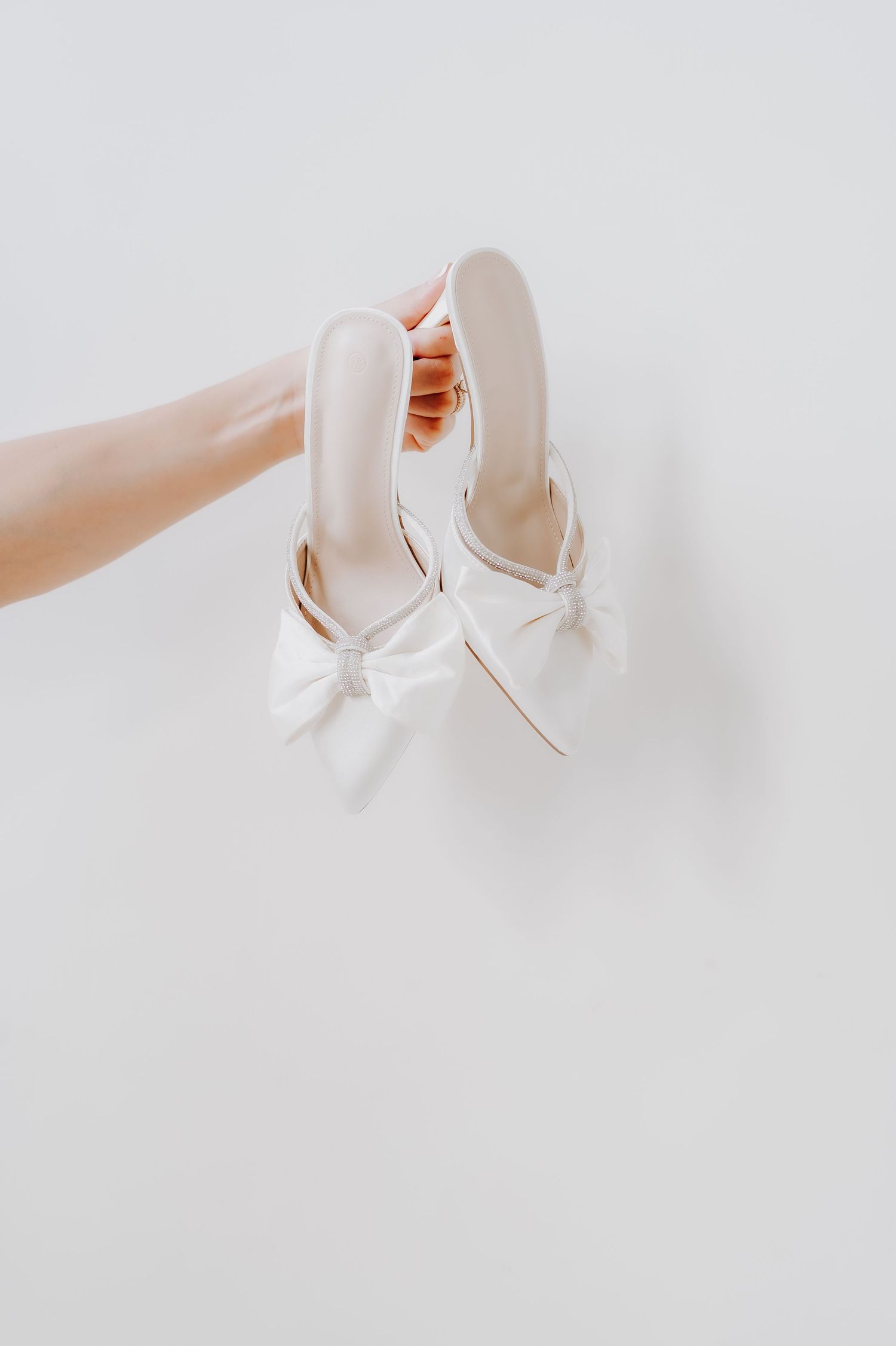 Elegant white bridal shoes with bow details held against a light background.