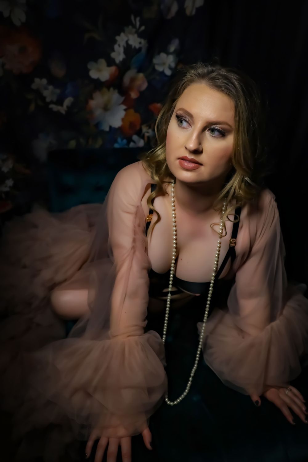 Vintage-style portrait with pearl necklace against dark floral background.