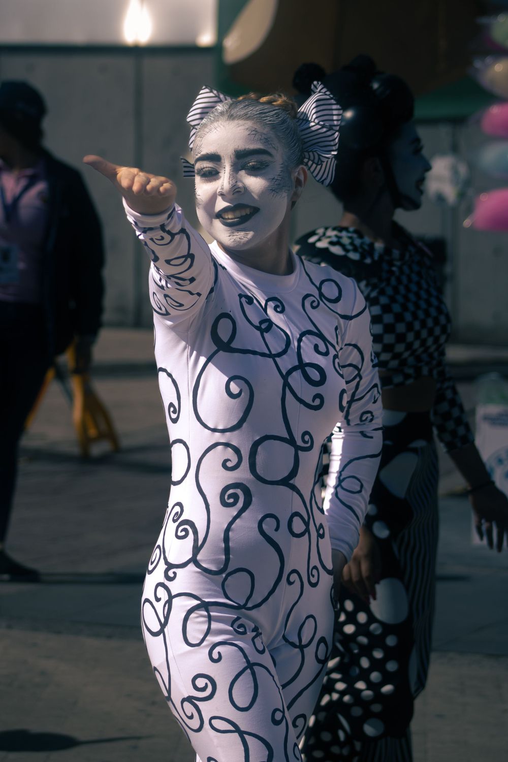 Female performer in black and white swirl bodysuit with face paint pointing at carnival.