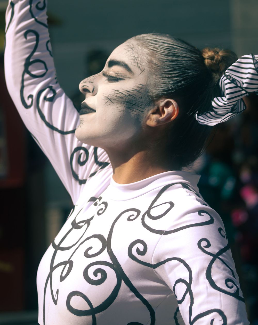 Female dancer with elaborate face paint and swirl costume performing with arm raised.